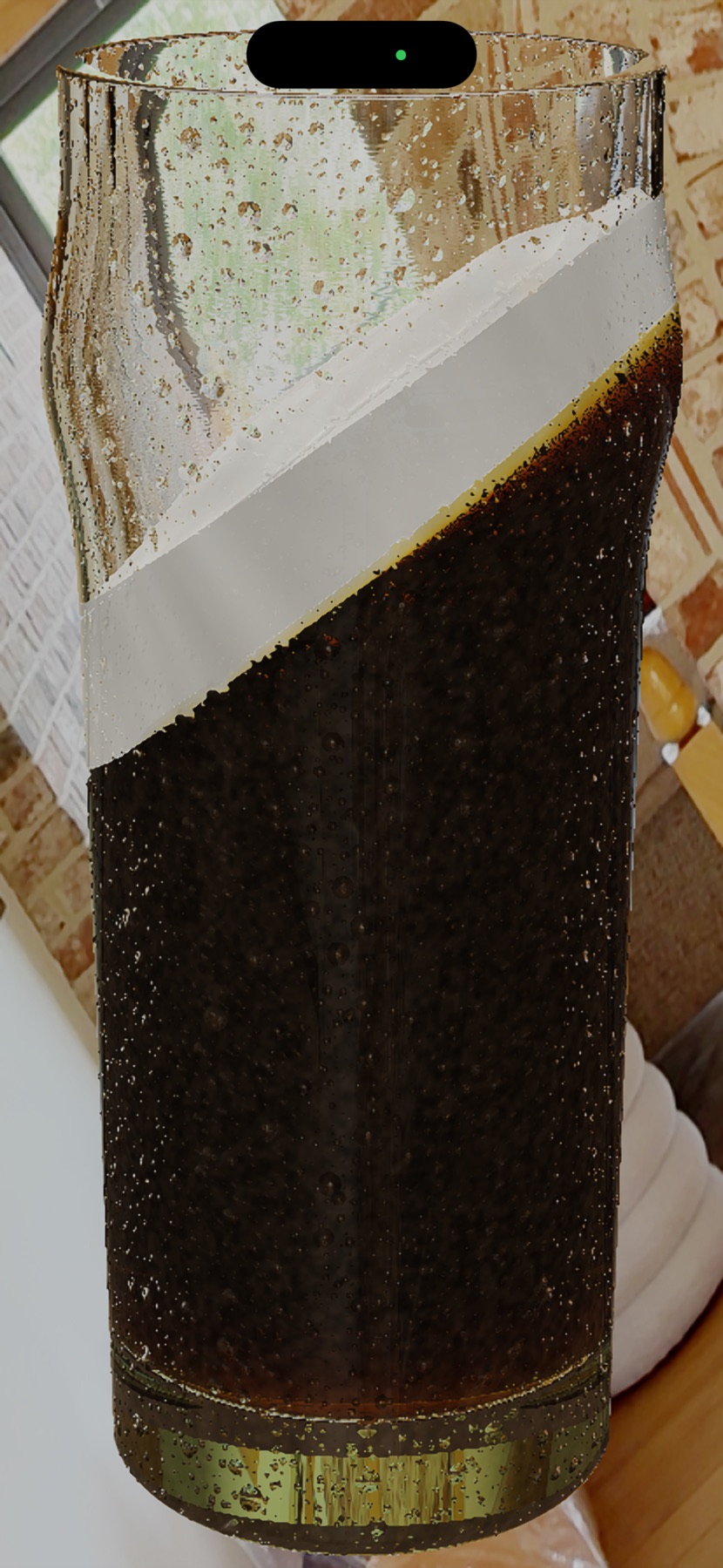 A stout glass tilted at a drinking angle, in front of a brick wall